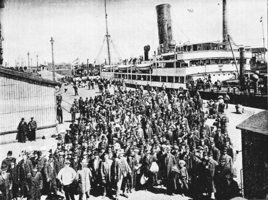 Historisches schwarz-weiss-Foto. Das Bild zeigt eine Menschenmasse, die dabei ist, in ein großes Schiff zu steigen.
