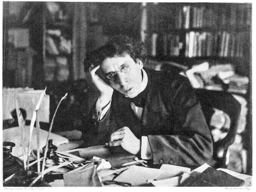 Historisches schwarz-weiss Bild von einem Mann, der an eiem Schreibtisch sitzt. Auf dem Tisch Papiere, im Hintergrund Bücher.