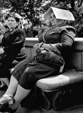 Schwarz-weiss-Fotografie von Fred Stein. Abgebildet wird eine Frau, die auf einer Bank in einem Park sitzt und sich mit einem Buch auf dem Kopf schatten macht.